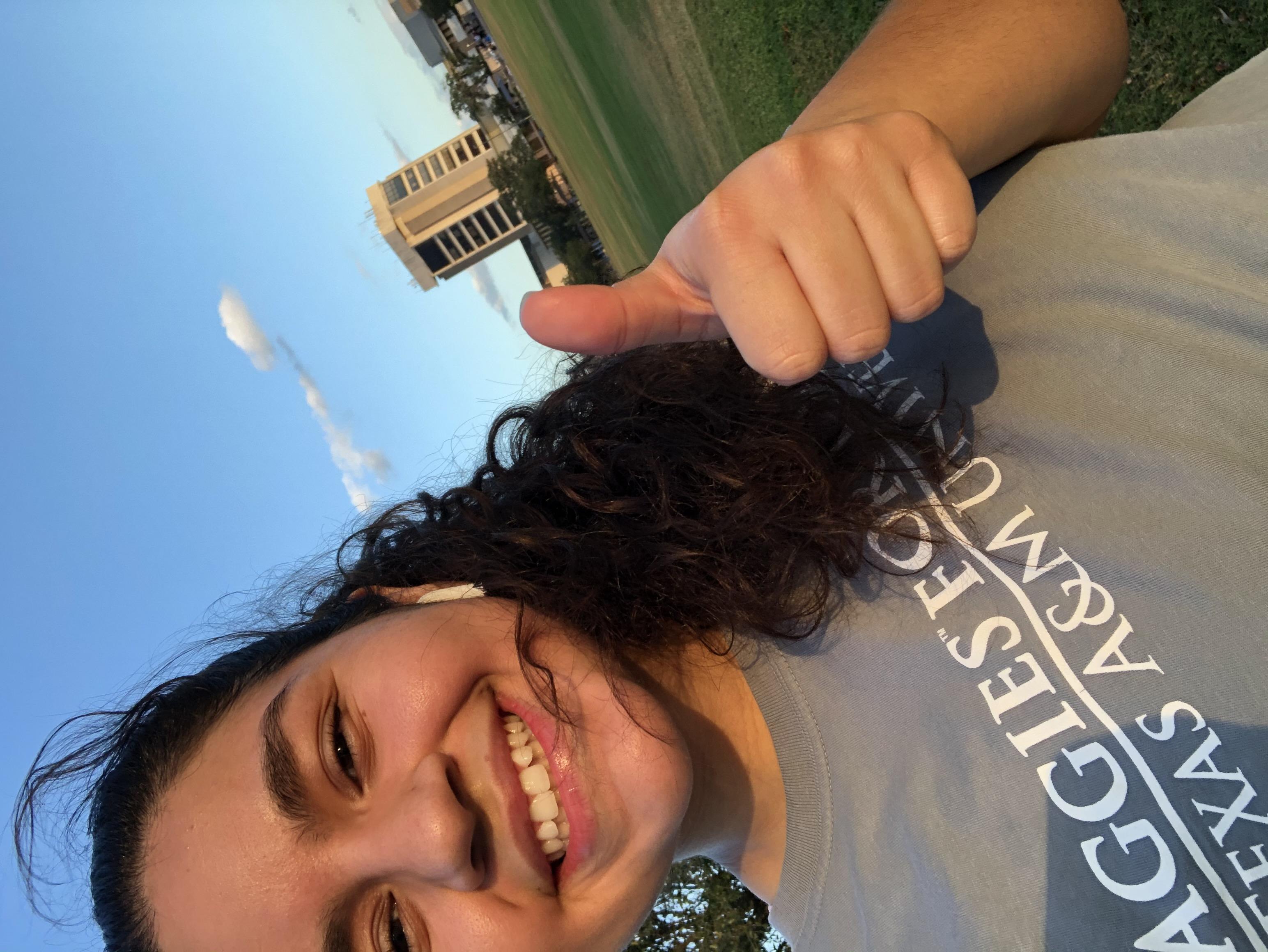 AFL member's selfie wearing organization t-shirt and giving thumbs up, with campus building visible in background